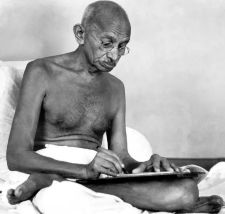 Mahatma Gandhi writing while seated on the floor